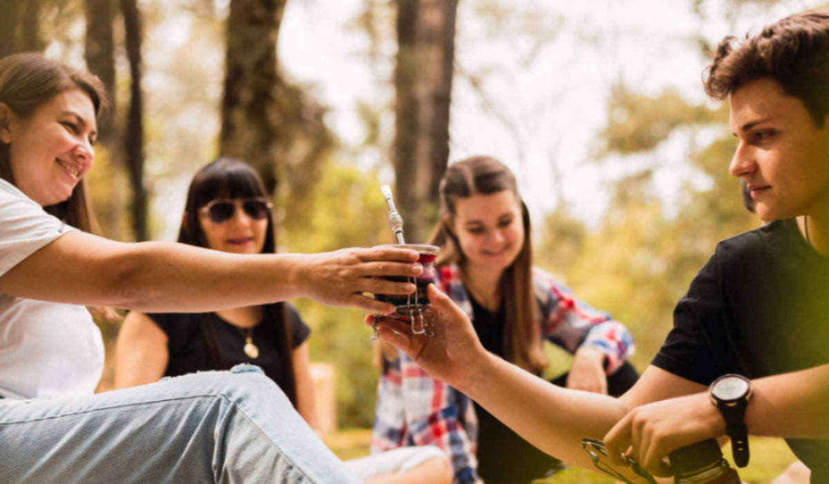 Two people exchanging a small bottle outdoors with friends in the background